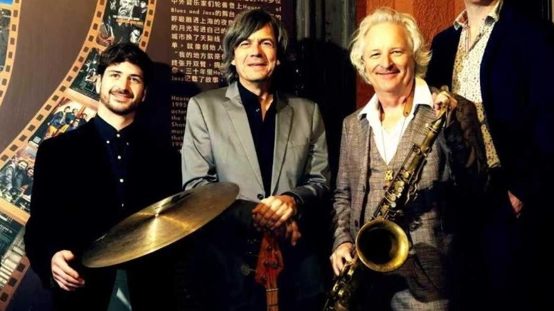 Vier M&auml;nner stehen l&auml;chelnd nebeneinander, einer h&auml;lt ein Saxophon, ein anderer ein Becken. Im Hintergrund ist eine dekorative Wand mit Schriftzeichen., &copy; Foto Peter Lehel Quartett