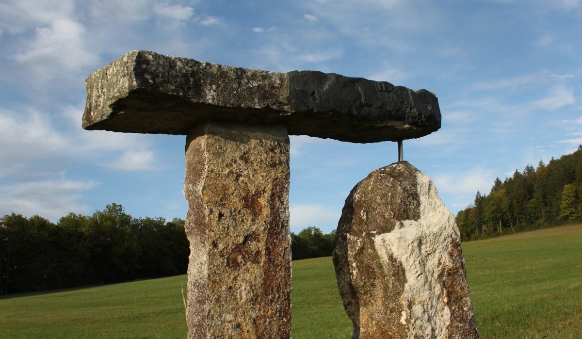 Eine Steinskulptur aus drei großen Steinen steht auf einer grünen Wiese unter einem blauen Himmel mit Wolken., © Touristik und Marketing GmbH Eine Steinskulptur aus drei großen Steinen steht auf einer grünen Wiese unter einem blauen Himmel mit Wolken., © Touristik und Marketing GmbH