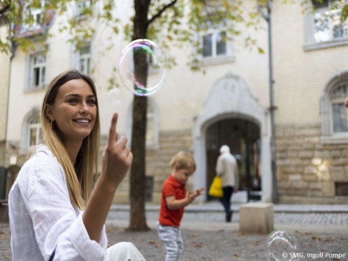 Eine Frau und ein Kind spielen mit Seifenblasen in einem gepflasterten Innenhof. Im Hintergrund sind B&auml;ume und ein Geb&auml;ude zu sehen., &copy; Stuttgart Marketing GmbH