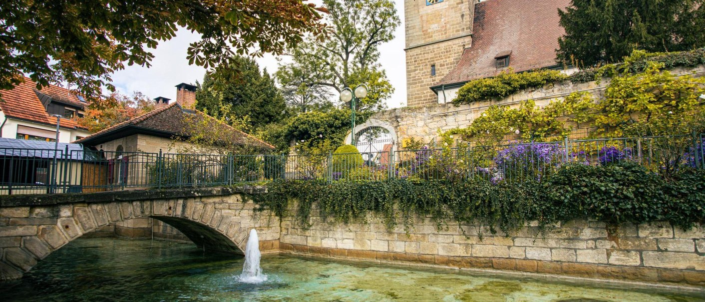 Ein idyllischer Blick auf die Innenstadt von Echterdingen mit einer Steinbrücke, einem Brunnen und einem historischen Turm im Hintergrund., © Stuttgart-Marketing GmbH, Sarah Schmid