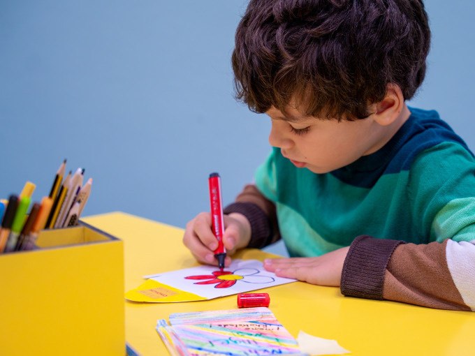 Ein Kind malt konzentriert mit einem roten Stift auf einem Blatt Papier an einem gelben Tisch. Im Hintergrund sind Buntstifte zu sehen., © Alfred Ritter GmbH & Co. KG | Waldenbuch Ein Kind malt konzentriert mit einem roten Stift auf einem Blatt Papier an einem gelben Tisch. Im Hintergrund sind Buntstifte zu sehen., © Alfred Ritter GmbH & Co. KG | Waldenbuch