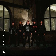 Fünf Personen in dunkler Kleidung posieren vor einem Gebäude mit großen Fenstern bei Nacht., © links im Bild