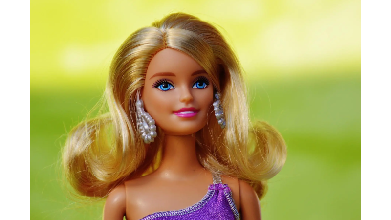 Barbie-Puppe mit blonden Haaren und lila Kleid, posiert vor einem unscharfen gr&uuml;nen Hintergrund. Sie tr&auml;gt auff&auml;llige Ohrringe., &copy; Pixabay, Alexa