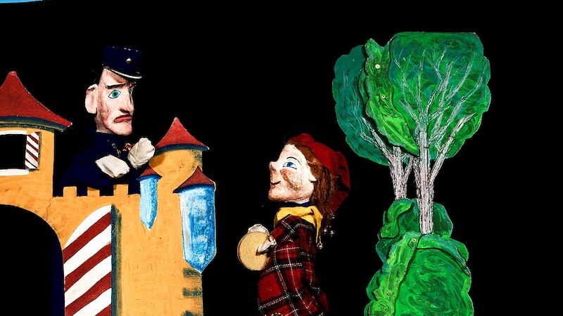 Zwei Puppenfiguren in einem Theaterst&uuml;ck. Eine Figur steht vor einem Schloss, die andere tr&auml;gt einen Korb. Im Hintergrund sind B&auml;ume zu sehen., &copy; Prinzessin Gisela Theater