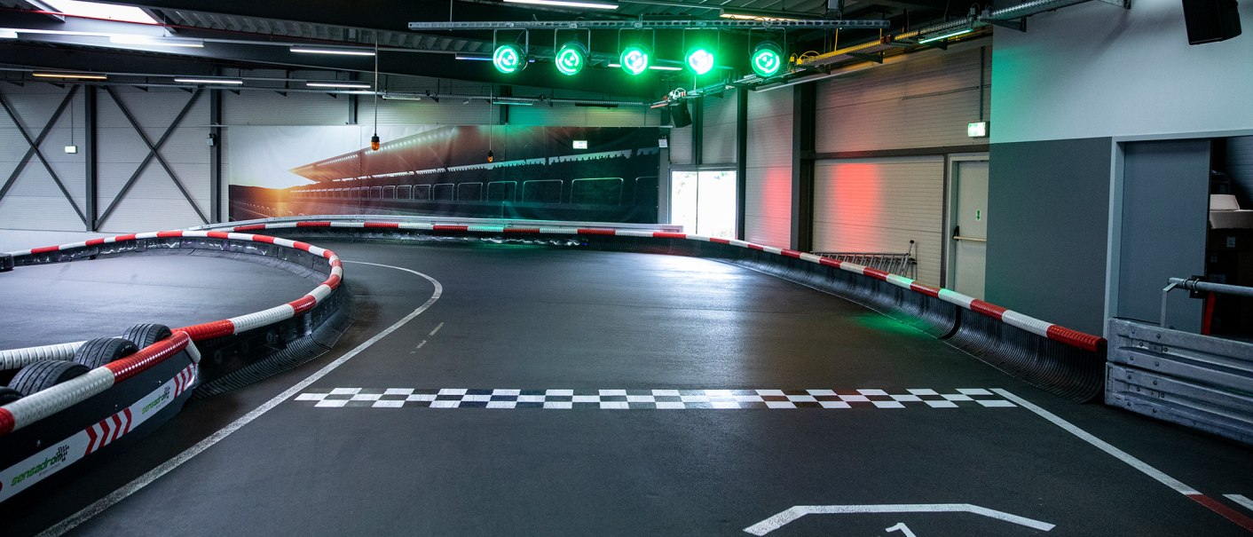 Kartbahn mit Start- und Ziellinie, Kurve, grünen Lichtern und Sicherheitsbarrieren in einer Halle., © Sensapolis GmbH Kartbahn mit Start- und Ziellinie, Kurve, grünen Lichtern und Sicherheitsbarrieren in einer Halle., © Sensapolis GmbH