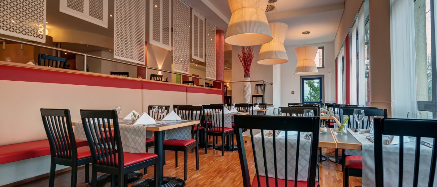 Modernes Restaurant mit roten und schwarzen Stühlen, weißen Tischdecken und großen Hängelampen. Elegante Atmosphäre mit Holzboden und großen Fenstern., © City Hotel Reutlingen