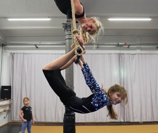 Zwei Mädchen üben Luftakrobatik an einem Seil in einer Turnhalle, während ein weiteres Kind zuschaut., © Kunstschule Labyrinth
