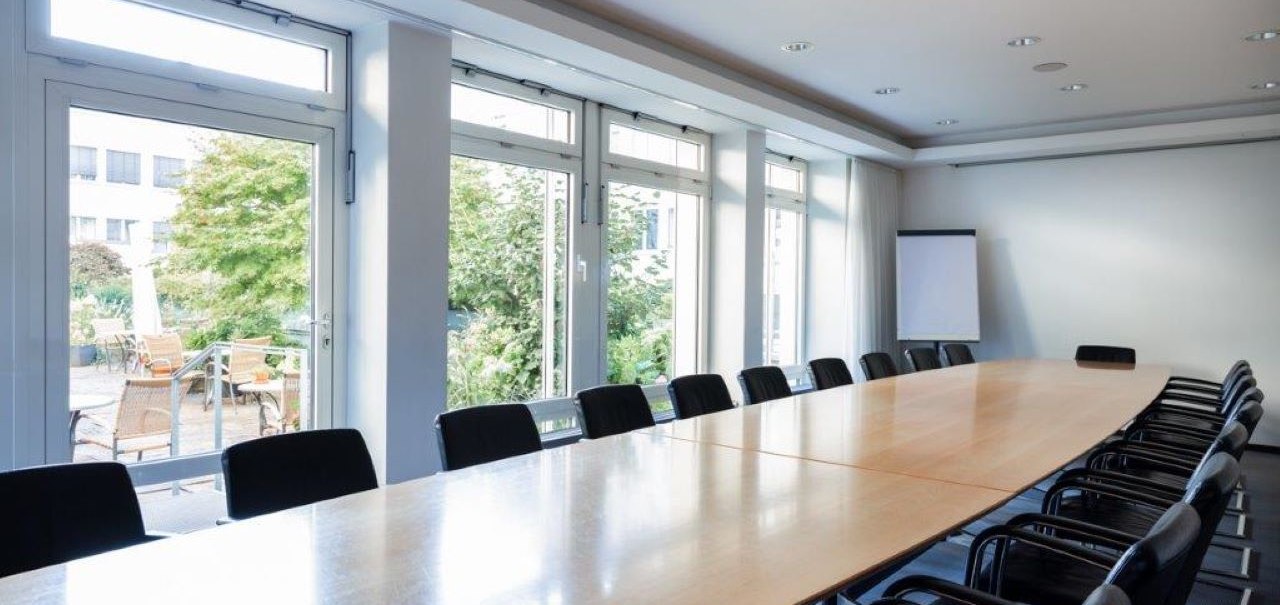 Leerer Tagungsraum mit langem Holztisch, schwarzen Stühlen und großen Fenstern, die auf eine Terrasse mit Pflanzen blicken., © Kronen Hotel GmbH