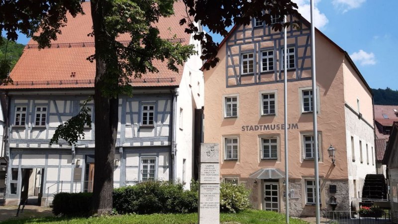 Das Stadtmuseum in einem historischen Fachwerkgeb&auml;ude bei sonnigem Wetter. Ein Baum und ein Denkmal stehen im Vordergrund., &copy; Stadt Bad Urach