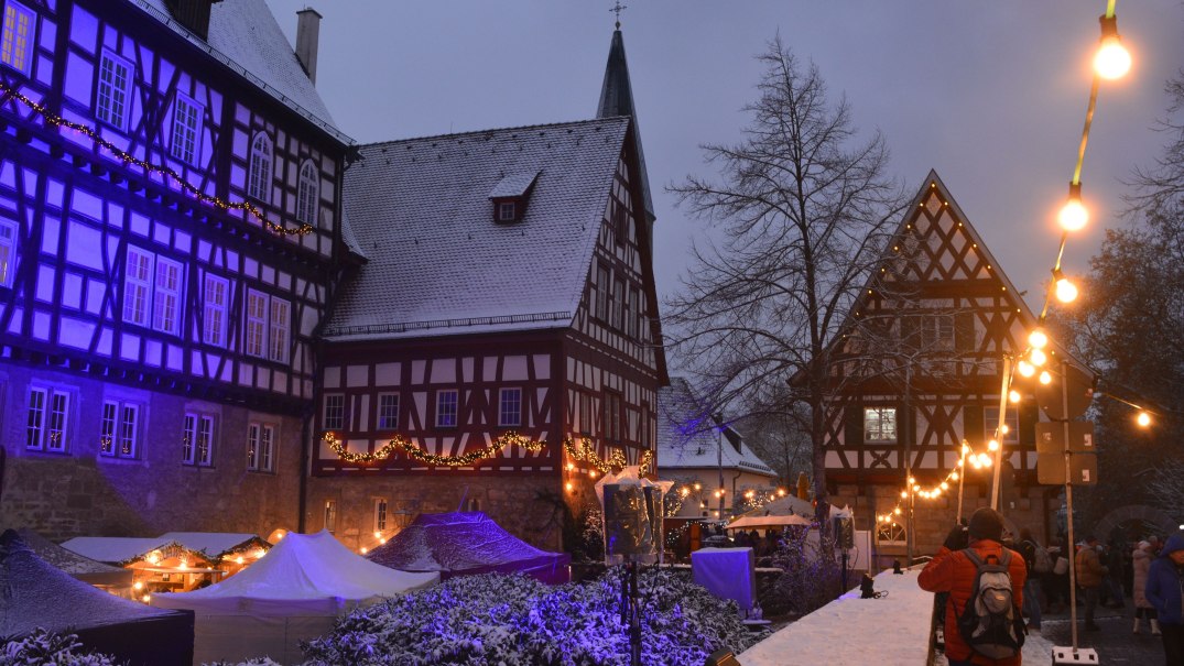Stimmungsvolles Weihnachtsmarktbild im Schnee: von blauem Licht angestrahltes Fachwerkgebäude, davor Hütten und Lichterketten, © Stadt Gaildorf Stimmungsvolles Weihnachtsmarktbild im Schnee: von blauem Licht angestrahltes Fachwerkgebäude, davor Hütten und Lichterketten, © Stadt Gaildorf
