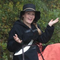 Eine Frau in mittelalterlicher Kleidung mit einem schwarzen Hut und einem Schwert posiert l&auml;chelnd im Wald., &copy; Copyright: Stefanie Keller