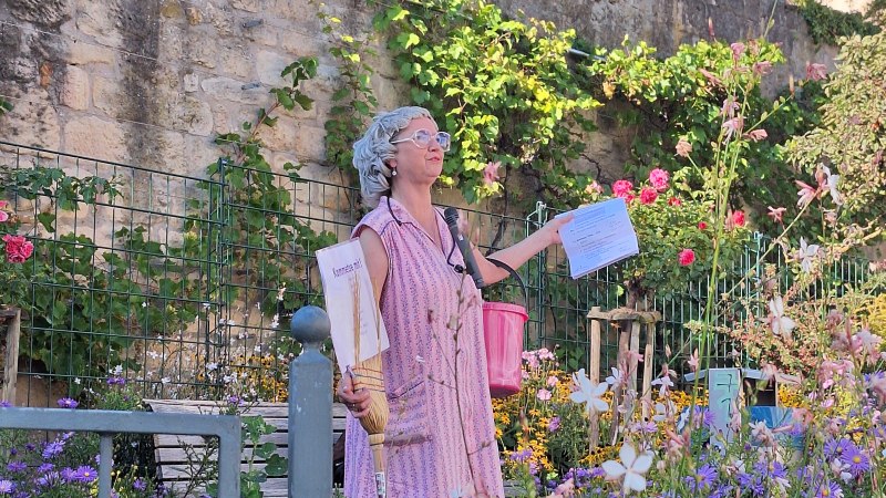 Eine als Putzfee „Frau Kunzle“ verkleidete Stadtführerin steht mit Besen, Kehrblech und pinkem Eimer in einem blühenden Garten vor einer historischen Steinmauer und einer Kirche. Sie hält ein Blatt in der Hand und erzählt während einer Stadtführung., © Stadt Leinfelden-Echterdingen | Yvonne Emhardt Eine als Putzfee „Frau Kunzle“ verkleidete Stadtführerin steht mit Besen, Kehrblech und pinkem Eimer in einem blühenden Garten vor einer historischen Steinmauer und einer Kirche. Sie hält ein Blatt in der Hand und erzählt während einer Stadtführung., © Stadt Leinfelden-Echterdingen | Yvonne Emhardt