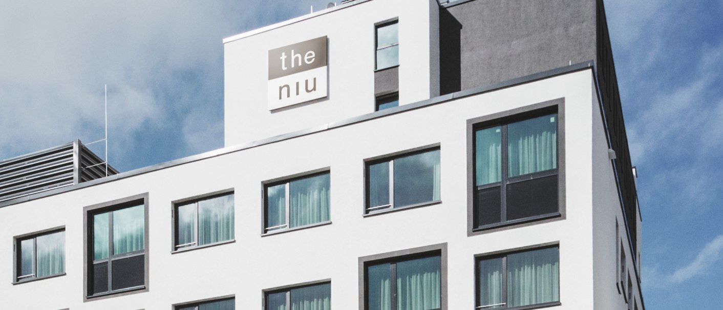 Moderne Hotelaußenfassade mit großen Fenstern und dem Logo "the niu" auf der oberen Etage., © the niu Form - Novum Hospitality
