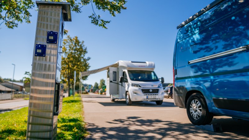 Wohnmobilstellplatz mit einem wei&szlig;en Wohnmobil und einem blauen Van. Im Vordergrund eine Stroms&auml;ule, im Hintergrund B&auml;ume und blauer Himmel., &copy; Stuttgart-Marketing GmbH, Thomas Niederm&uuml;ller