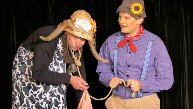 Zwei Männer in Kostümen auf einer Bühne, einer als Kuh verkleidet, der andere mit Hut und Sonnenblume., © Galli Theater Backnang