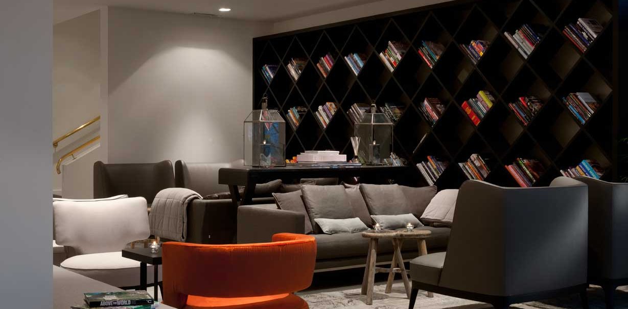 Moderne Lobby mit gemütlichen Sofas, einem großen Bücherregal und stilvollen Dekorationen. Einladende Atmosphäre mit gedämpfter Beleuchtung., © Wyndham Stuttgart Airport Messe