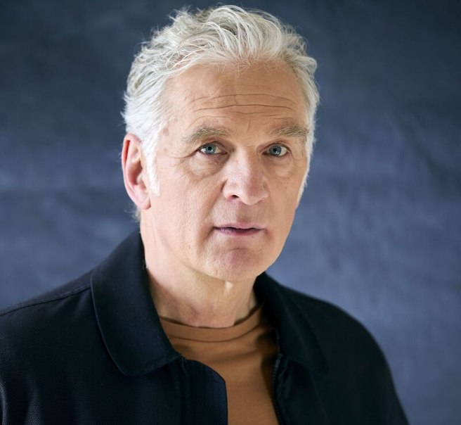 Ein &auml;lterer Mann mit grauem Haar und nachdenklichem Ausdruck blickt in die Kamera. Er tr&auml;gt eine dunkle Jacke und ein braunes Shirt vor einem dunklen Hintergrund., &copy; Stadthalle Leonberg