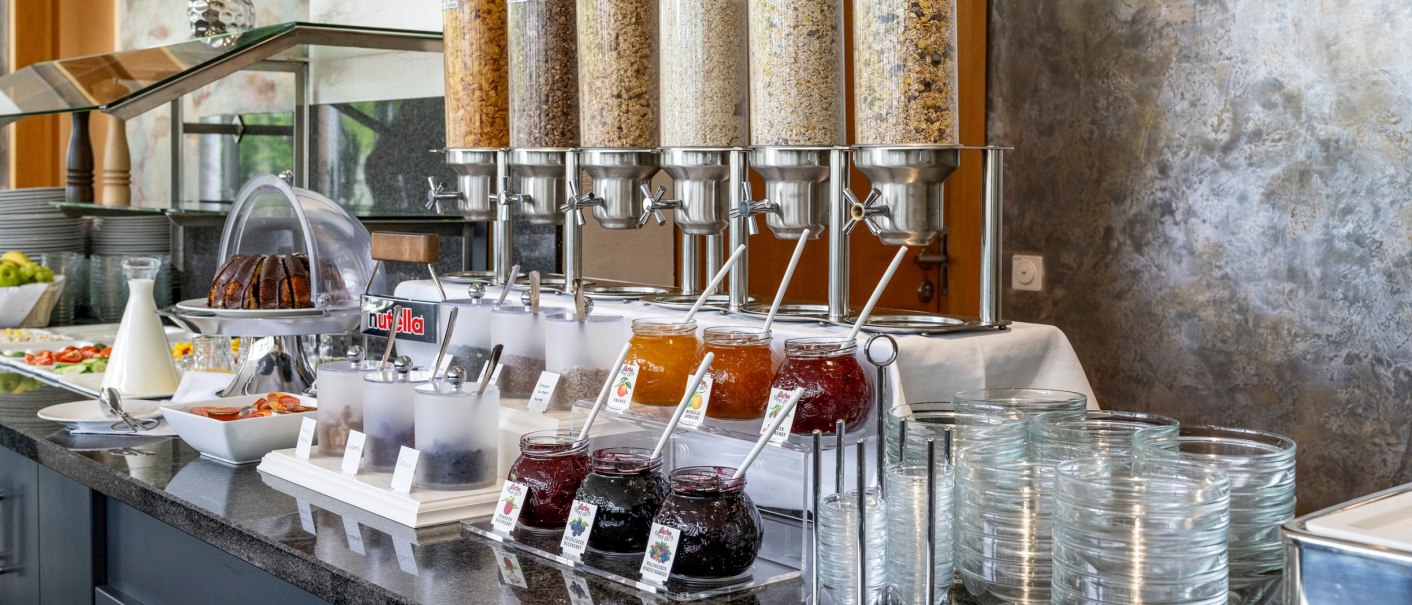 Ein Frühstücksbuffet mit verschiedenen Müslisorten, Marmeladen, Nutella, Milch und frischem Obst auf einer Theke., © Plaza Residence Stuttgart-Ditzingen Ein Frühstücksbuffet mit verschiedenen Müslisorten, Marmeladen, Nutella, Milch und frischem Obst auf einer Theke., © Plaza Residence Stuttgart-Ditzingen