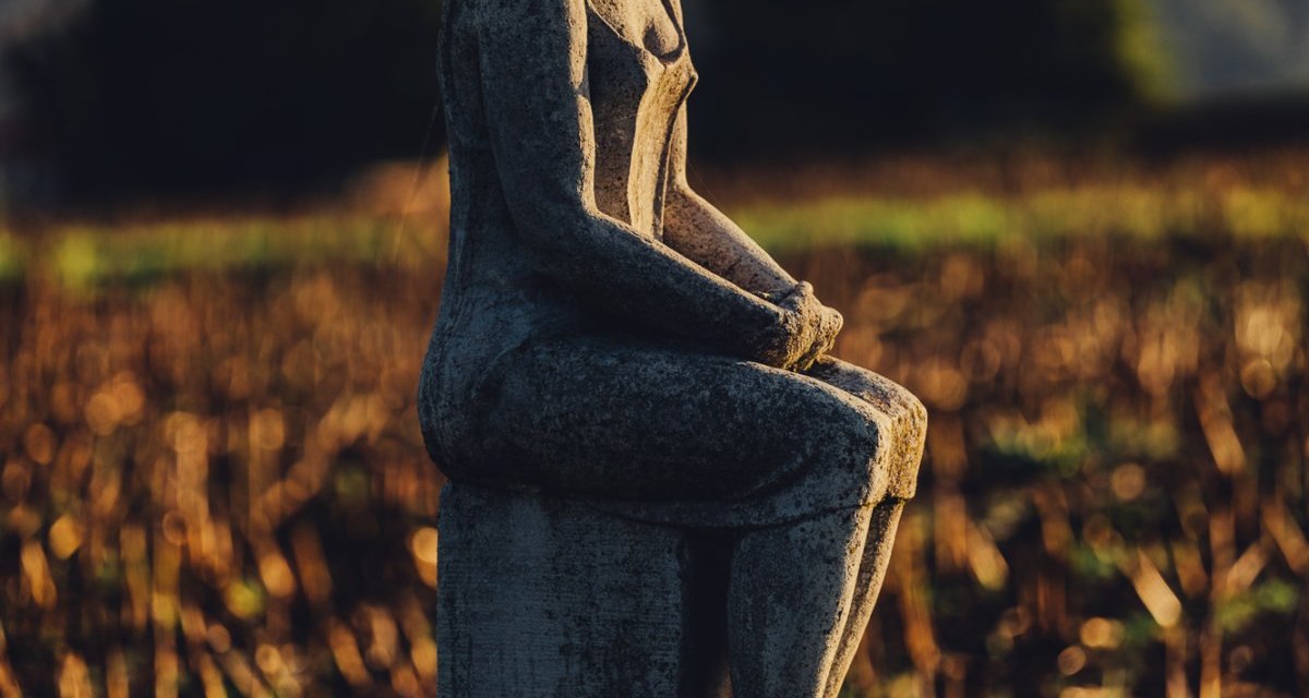 Steinskulptur einer sitzenden Frau auf einem Feld, beleuchtet von warmem Sonnenlicht. Im Hintergrund sind Bäume und ein Hügel zu sehen., © Landratsamt Ostalbkreis Steinskulptur einer sitzenden Frau auf einem Feld, beleuchtet von warmem Sonnenlicht. Im Hintergrund sind Bäume und ein Hügel zu sehen., © Landratsamt Ostalbkreis