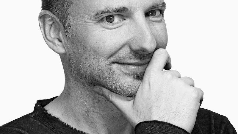 Schwarz-weiß Porträt eines Mannes, der lächelnd in die Kamera schaut und seine Hand nachdenklich ans Kinn legt., © Mauerwerk GmbH