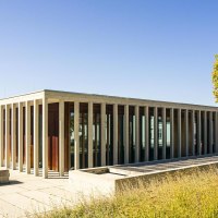 Modernes Gebäude mit Glasfassade und Säulen, umgeben von Bäumen und Wiese unter klarem Himmel., © SMG, Sarah Schmid Modernes Gebäude mit Glasfassade und Säulen, umgeben von Bäumen und Wiese unter klarem Himmel., © SMG, Sarah Schmid