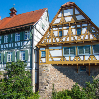Fachwerkhäuser mit roten Dächern und grünen Fensterläden, umgeben von Bäumen, unter klarem blauem Himmel., © Stuttgart-Marketing GmbH, Achim Mende Fachwerkhäuser mit roten Dächern und grünen Fensterläden, umgeben von Bäumen, unter klarem blauem Himmel., © Stuttgart-Marketing GmbH, Achim Mende