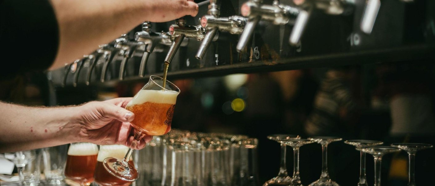 Ein Glas Bier wird an einem Zapfhahn gefüllt. Im Hintergrund sind weitere Gläser und Zapfhähne zu sehen., © Kraftpaule