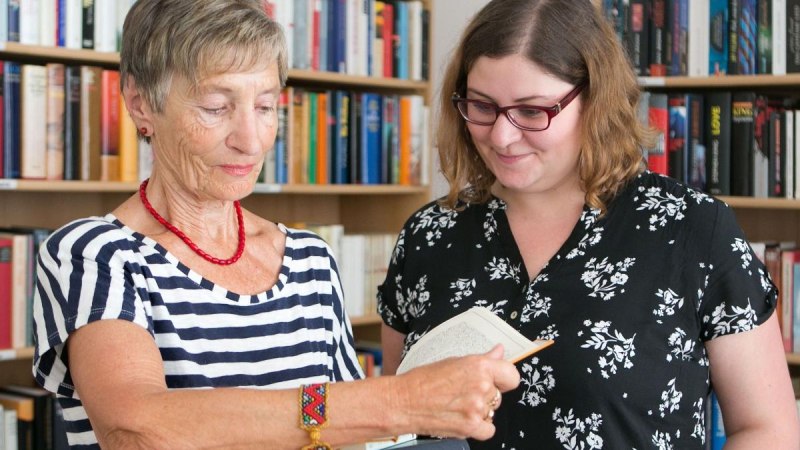 Zwei Frauen stehen vor einem Bücherregal. Eine ältere Frau zeigt einer jüngeren Frau ein Buch. Beide wirken interessiert und freundlich., © Bürgerengagement und Bürgerhäuser Zwei Frauen stehen vor einem Bücherregal. Eine ältere Frau zeigt einer jüngeren Frau ein Buch. Beide wirken interessiert und freundlich., © Bürgerengagement und Bürgerhäuser