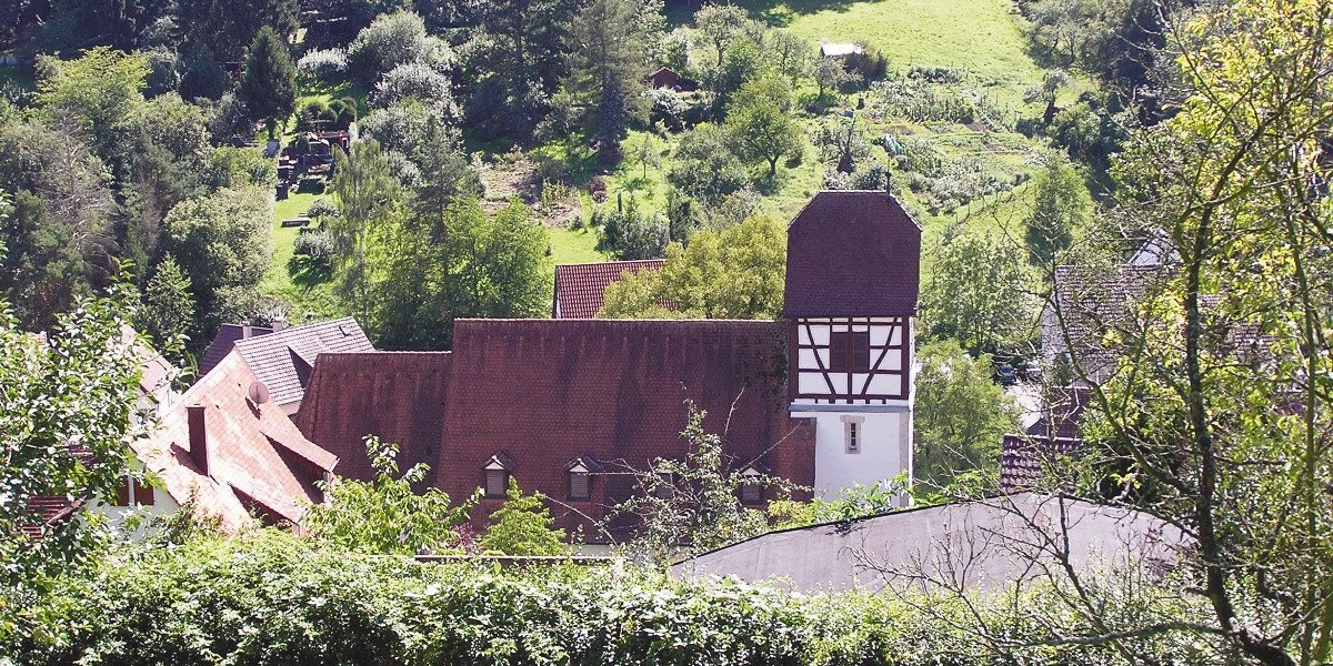 Ein Fachwerkhaus mit rotem Dach in einer grünen, ländlichen Umgebung. Im Hintergrund sind Gärten und Bäume zu sehen., © Stuttgart-Marketing GmbH Ein Fachwerkhaus mit rotem Dach in einer grünen, ländlichen Umgebung. Im Hintergrund sind Gärten und Bäume zu sehen., © Stuttgart-Marketing GmbH