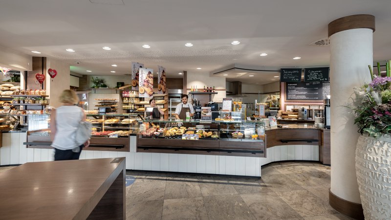 Eine B&auml;ckerei mit Theke voller Backwaren. Zwei Mitarbeiter bedienen Kunden. Die Einrichtung ist modern und einladend., &copy; Tr&ouml;lsch GmbH