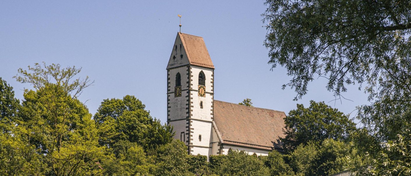 Die St. Blasius Kirche in Plochingen erhebt sich majestätisch über die umgebenden Bäume unter einem klaren blauen Himmel., © SMG, Sarah Schmid Die St. Blasius Kirche in Plochingen erhebt sich majestätisch über die umgebenden Bäume unter einem klaren blauen Himmel., © SMG, Sarah Schmid
