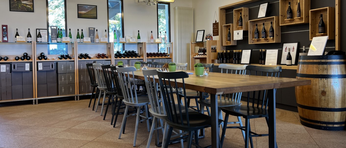 Vinothek mit Holztisch und Stühlen, umgeben von Weinregalen und Dekoration. Helle, einladende Atmosphäre mit Weinflaschen und Pflanzen., © Weinfactum Bad Cannstatt Vinothek mit Holztisch und Stühlen, umgeben von Weinregalen und Dekoration. Helle, einladende Atmosphäre mit Weinflaschen und Pflanzen., © Weinfactum Bad Cannstatt