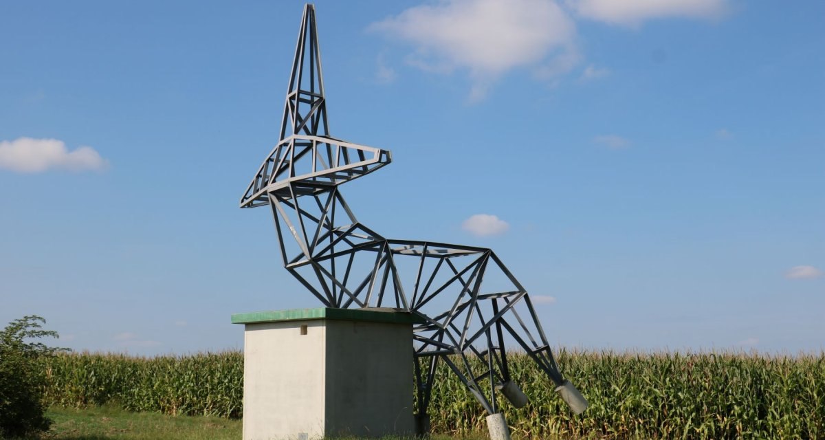 Metallskulptur eines stilisierten Rehs auf einem Betonsockel vor einem Maisfeld und blauem Himmel., © Remstal Tourismus e.V. Metallskulptur eines stilisierten Rehs auf einem Betonsockel vor einem Maisfeld und blauem Himmel., © Remstal Tourismus e.V.