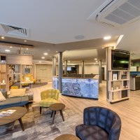 Moderne Hotellobby mit gemütlichen Sitzgelegenheiten, Regalen und einer Rezeption. Helle Beleuchtung und stilvolle Einrichtung dominieren den Raum., © TOMAS