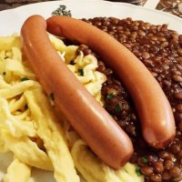Ein Teller mit Linsen, Spätzle und zwei Würstchen, serviert auf einem Tisch mit Besteck., © TMBW, Susi Maier