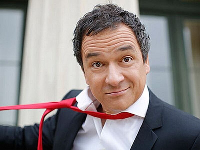 Ein Mann in einem Anzug zieht spielerisch an seiner roten Krawatte und schaut in die Kamera. Der Hintergrund ist unscharf., © Stadthalle Leonberg Ein Mann in einem Anzug zieht spielerisch an seiner roten Krawatte und schaut in die Kamera. Der Hintergrund ist unscharf., © Stadthalle Leonberg