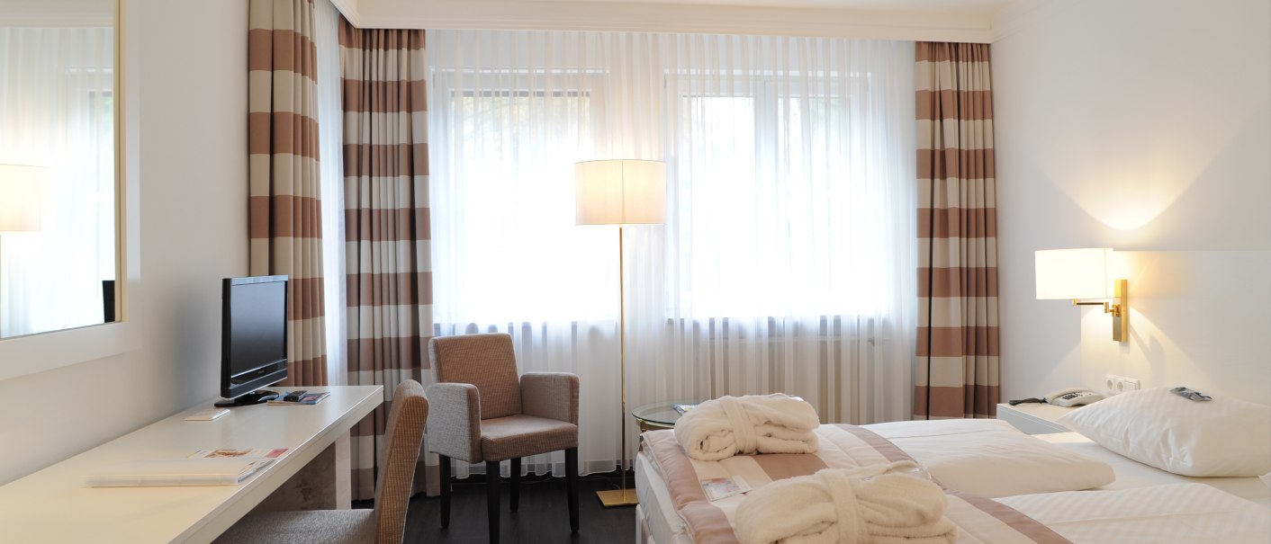 Helles Doppelzimmer mit modernem Design, Doppelbett, Schreibtisch, Fernseher und Sessel. Große Fenster mit gestreiften Vorhängen., © relexa Waldhotel Schatten Helles Doppelzimmer mit modernem Design, Doppelbett, Schreibtisch, Fernseher und Sessel. Große Fenster mit gestreiften Vorhängen., © relexa Waldhotel Schatten