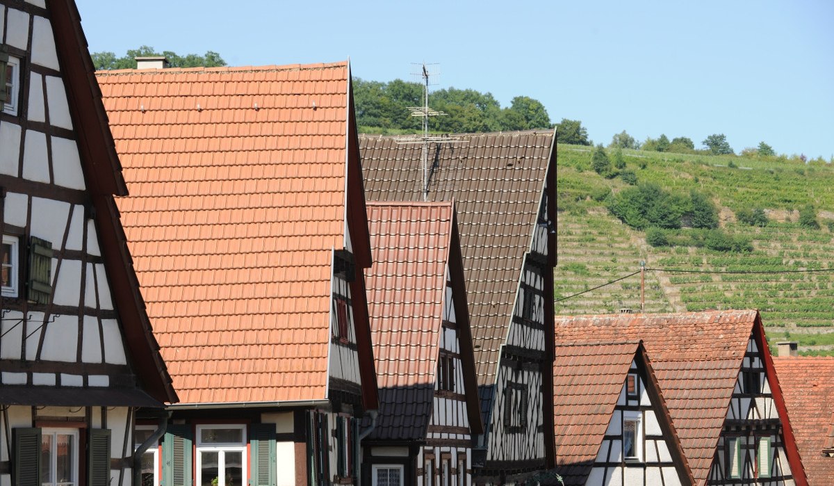 Fachwerkhäuser mit roten Ziegeldächern in Roßwag, im Hintergrund grüne Weinberge unter blauem Himmel., © Land der 1000 Hügel - Kraichgau-Stromberg