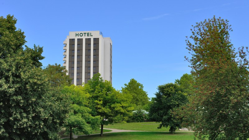 Hotelgeb&auml;ude hinter B&auml;umen in einem Park, blauer Himmel., &copy; AMBER HOTEL Leonberg / Stuttgart