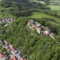 Luftaufnahme der Burgruine Rechberg in Schwäbisch Gmünd, umgeben von grünen Wäldern und einem kleinen Dorf. Felder und Wälder erstrecken sich im Hintergrund., © Burg Rechberg