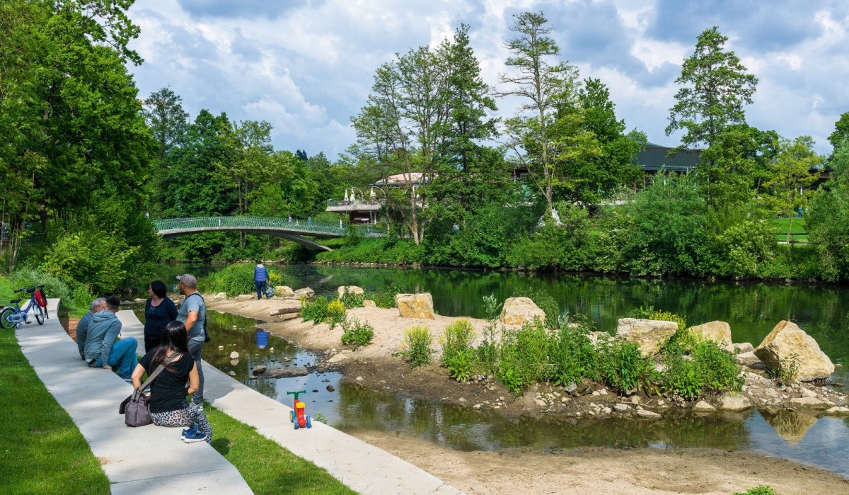 Menschen entspannen an einem Flussufer in einem grünen Park. Eine Brücke und Bäume sind im Hintergrund zu sehen., © Remstal Tourismus e.V. Menschen entspannen an einem Flussufer in einem grünen Park. Eine Brücke und Bäume sind im Hintergrund zu sehen., © Remstal Tourismus e.V.
