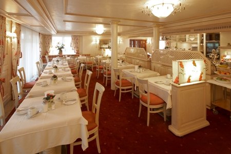 Eleganter Frühstücksraum mit weißen Tischdecken, roten Stühlen und dekorativen Leuchten. Ein Buffetbereich ist im Hintergrund sichtbar., © Jeanette Bender Eleganter Frühstücksraum mit weißen Tischdecken, roten Stühlen und dekorativen Leuchten. Ein Buffetbereich ist im Hintergrund sichtbar., © Jeanette Bender