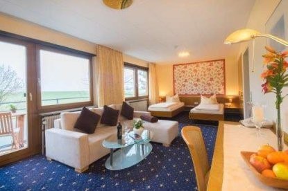 Helles Hotelzimmer mit zwei Betten, Sofa, Glastisch und Balkon. Blumenmuster an der Wand, Obstschale und Lampe auf dem Tisch., © Kemnater Hof