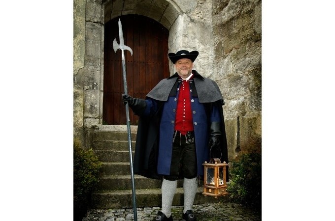 Ein Mann in historischer Nachtwächterkleidung mit Hellebarde und Laterne steht vor einer alten Steintür., © Stadt Murrhardt