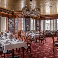 Elegantes Steakhouse mit weißen Tischdecken, Holzstühlen und Kronleuchter. Roter Teppichboden und große Fenster sorgen für eine warme Atmosphäre., © copyright by Kilian Blees