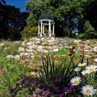 Ein blühender Garten mit bunten Blumen, einem kleinen Teich und einem Pavillon im Hintergrund, umgeben von Bäumen., © Staatsministerium Baden-Württemberg Ein blühender Garten mit bunten Blumen, einem kleinen Teich und einem Pavillon im Hintergrund, umgeben von Bäumen., © Staatsministerium Baden-Württemberg