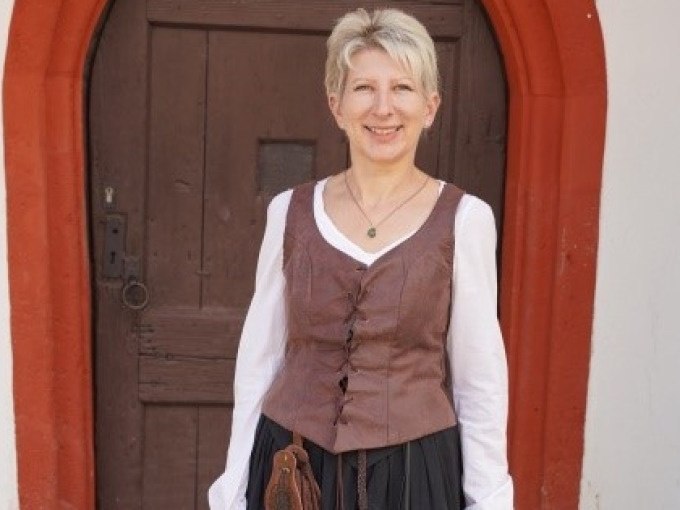 Eine Frau in historischer Kleidung steht l&auml;chelnd vor einer alten Holzt&uuml;r mit rotem Rahmen., &copy; Stadtverwaltung Weil der Stadt