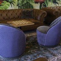 Gemütliche Sitzecke mit braunen Ledersofas, blauen Sesseln und einem Schachbrett-Tisch vor einer Wand mit tropischem Pflanzenmuster., © 13 6 Design GmbH (Judenhof 10, 89073 Ulm) Gemütliche Sitzecke mit braunen Ledersofas, blauen Sesseln und einem Schachbrett-Tisch vor einer Wand mit tropischem Pflanzenmuster., © 13 6 Design GmbH (Judenhof 10, 89073 Ulm)