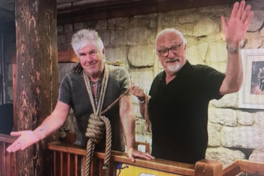 Zwei Männer stehen in einem rustikalen Raum. Einer hat ein Seil um den Hals, beide lächeln und gestikulieren freundlich., © Kabarett der Galgenstricke