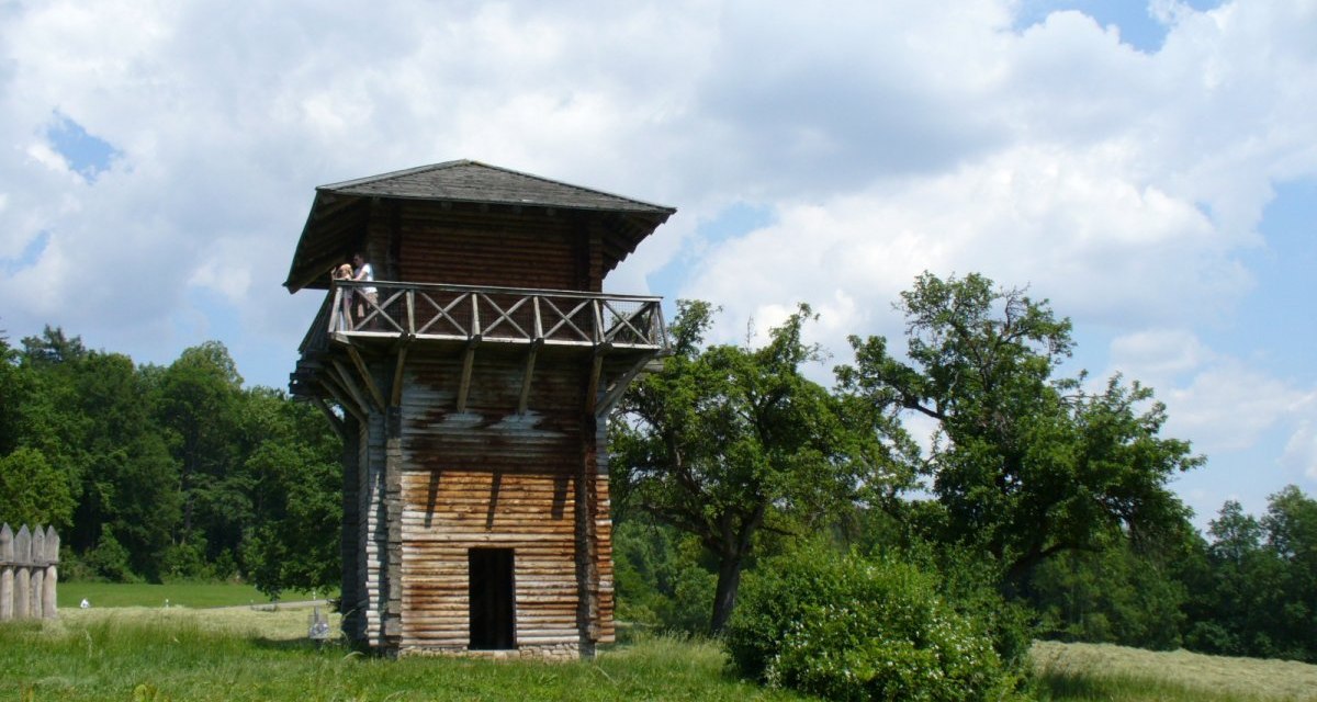 Ein hölzerner römischer Wachturm auf einer Wiese, umgeben von Bäumen und einem bewölkten Himmel. Ein hölzerner römischer Wachturm auf einer Wiese, umgeben von Bäumen und einem bewölkten Himmel.